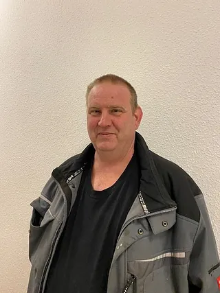 Ein Mann in Arbeitsjacke lächelt leicht.