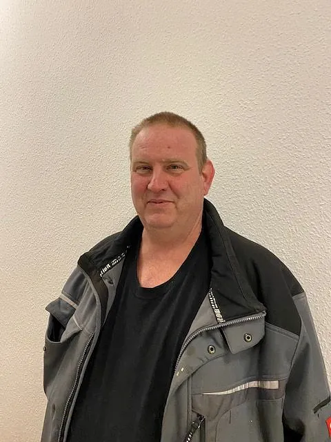 Ein Mann in Arbeitsjacke lächelt leicht.