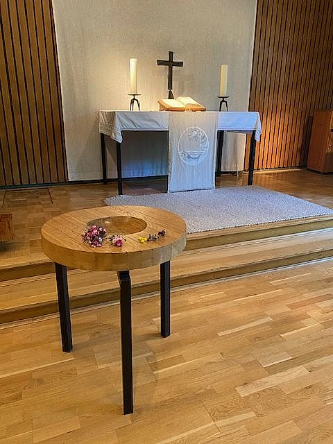 Altar mit Kerzen und Kreuz, kleiner Tisch mit Blumen.