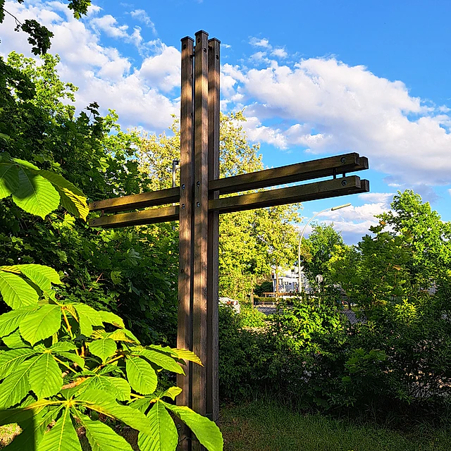 Ein großes Holzkreuz steht zwischen grünen Bäumen.