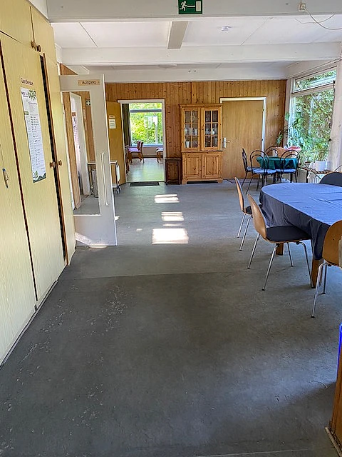 Gemeindesaal mit Tischen und offener Tür.